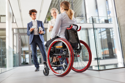 A person in a wheelchair converses with two standing people in the company building